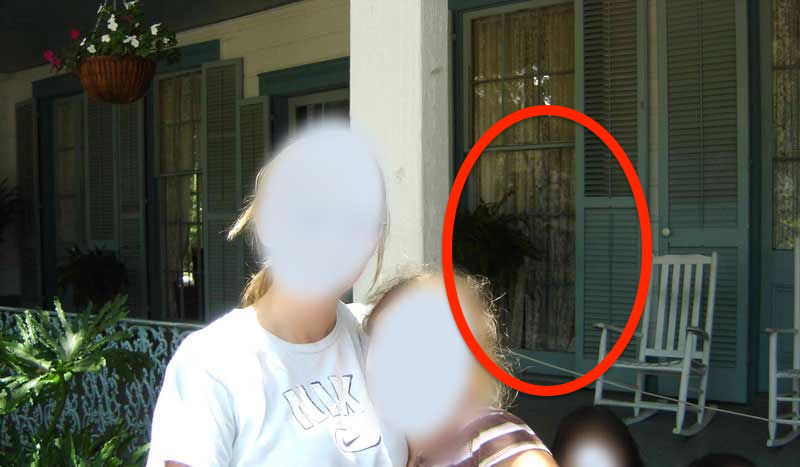 A teacher and two students, with their faces blurred, posing at The Myrtles Plantation with a ghostly figure of a girl looking through the window behind them